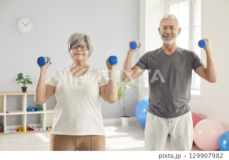 Happy Elderly Couple Exercising With Dumbbells In Gym 129907982
