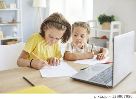 Two focused preteen children sitting together at table, drawing and enjoying creative activities. Two focused preteen children sitting together at table, drawing and enjoying creative activities. 129907986