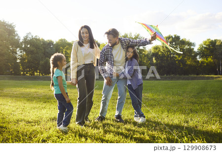 Summer green park, family standing smiling warmly holding preparing colorful kite for flying, joyful 129908673