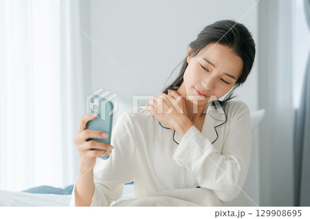 寝起きでスマホを見る女性 129908695