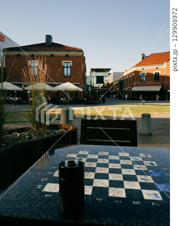 Chessboard embedded in urban outdoor table, surrounding revitalised architecture with cafes and shops, bathing in golden afternoon sunlight in Polish cityscape. Kazimierz district in Krakow, Poland Chessboard embedded in urban outdoor table, surrounding revitalised architecture with cafes and shops, bathing in golden afternoon sunlight in Polish cityscape. Kazimierz district in Krakow, Poland 129908972