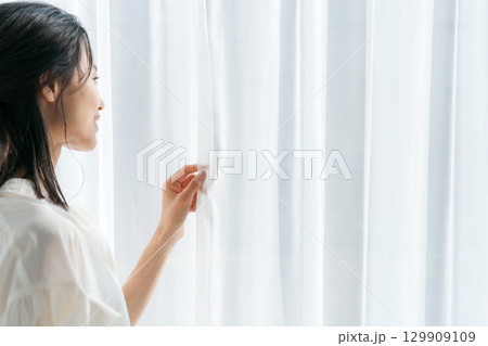 窓際に立ってカーテンを開ける女性 129909109