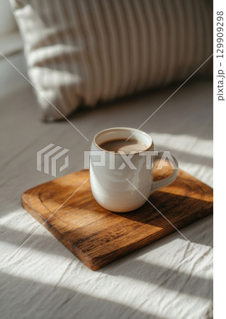 Ceramic Coffee Mug Resting on a Wooden Tray in Soft Morning Light on a Cozy Bed 129909298