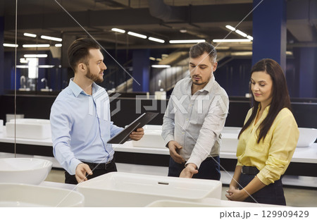 Family couple choosing sink for bathroom in bath store, listening advice of shop assistant  129909429