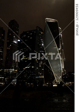 City skyline featuring modern skyscrapers illuminated at night near the waterfront in a bustling urban environment 129909458