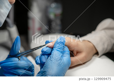 Nail technician performing manicure with precision tools in a modern salon setting 129909475