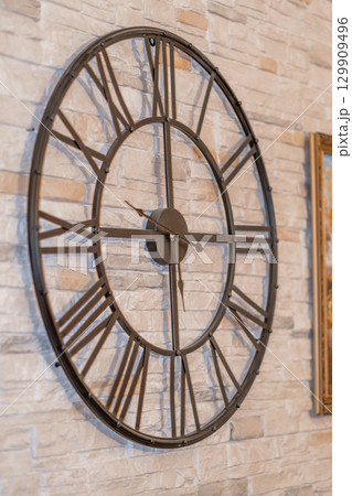 Large wall clock with Roman numerals against a textured stone background in a modern interior design setting Large wall clock with Roman numerals against a textured stone background in a modern interior design setting 129909496