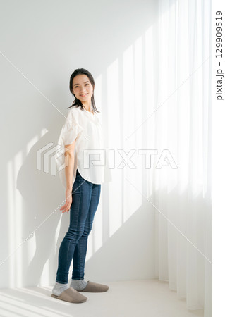 窓辺に立つデニムの女性（縦長） 129909519