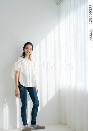 窓辺に立つデニムの女性（縦長） 129909527