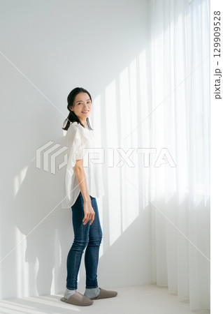 窓辺に立つデニムの女性（縦長） 129909528