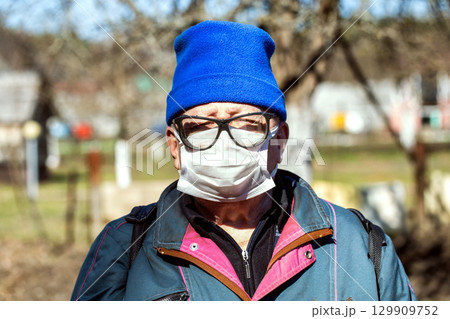 elderly man in glasses and blue cap and protective medical mask. Concept of protection from viruses and bacteria, epidemic. Humor, close-up 129909752