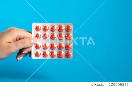 Blister with red pills in hand on blue background. Concept of chondroprotector pills for joint health. Copy space for text, painkillers Blister with red pills in hand on blue background. Concept of chondroprotector pills for joint health. Copy space for text, painkillers 129909835
