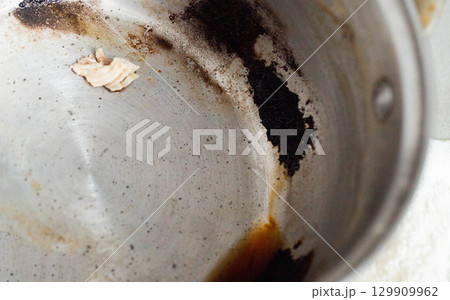 Burnt food in a saucepan, close-up. Black burnt food deposits on non-stick coating, harm Burnt food in a saucepan, close-up. Black burnt food deposits on non-stick coating, harm 129909962