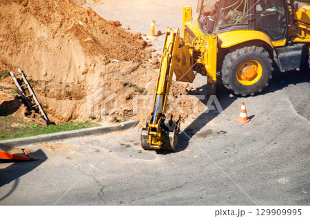 Modern yellow forklift stands on the road near the dug up road. Concept of emergency service for elimination of accident in water supply and sewerage. Copy space for text Modern yellow forklift stands on the road near the dug up road. Concept of emergency service for elimination of accident in water supply and sewerage. Copy space for text 129909995
