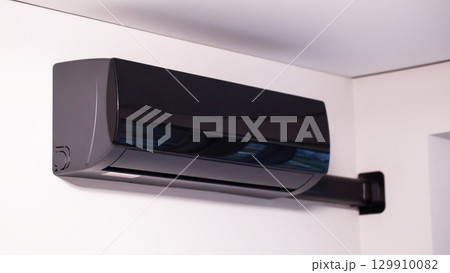 Modern black air conditioner on white wall in room, close-up 129910082