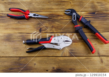 Set of different pliers on wooden background. Top view 129910154