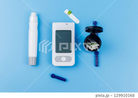 Digital glucometer, lancet pen, disposable needles and test strips on pastel blue background. Top view. Diabetes concept 129910168