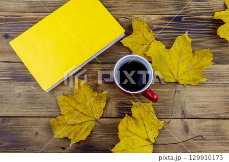 Cup of coffee, book and autumn maple leaves on wooden table. Top view. Autumn cozy concept Cup of coffee, book and autumn maple leaves on wooden table. Top view. Autumn cozy concept 129910173