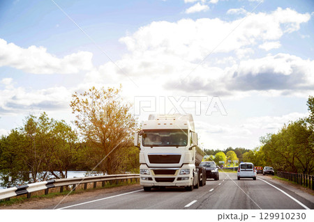Tanker truck transports milk along country road against forest and sun in summer. Copy space for text, agriculture. Beautiful sky 129910230