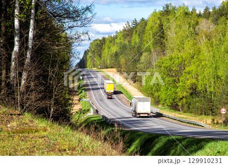 A convoy of trucks transports cargo uphill against a forest in the summer. Transport and logistics company for cargo delivery. Cargo insurance as a business, industry A convoy of trucks transports cargo uphill against a forest in the summer. Transport and logistics company for cargo delivery. Cargo insurance as a business, industry 129910231