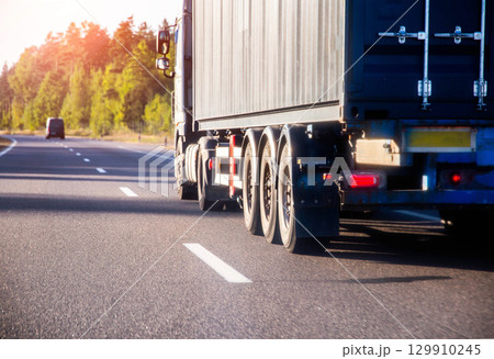 Container truck tractor transports sea container with cargo on asphalt road against forest and nature background. Copy space for text Container truck tractor transports sea container with cargo on asphalt road against forest and nature background. Copy space for text 129910245