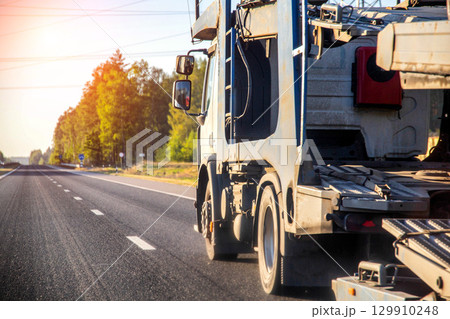 Modern tractor for transporting cars on a summer road at sunset, industry Modern tractor for transporting cars on a summer road at sunset, industry 129910248