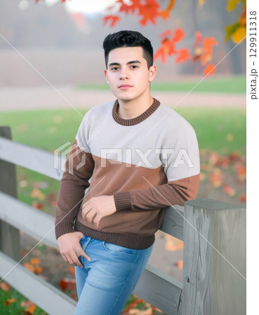 Young Man Posing in Brown and Gray Sweater Leaning on a Wooden Fence Amid Autumn Leaves Young Man Posing in Brown and Gray Sweater Leaning on a Wooden Fence Amid Autumn Leaves 129911318