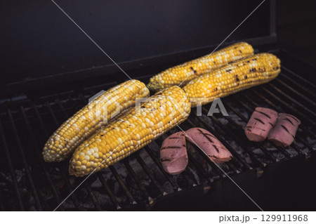 Grilled corn on the cob and sausage ready for a summer barbecue. A close-up shot of corn on the cob and sausage grilling on a barbecue grill. 129911968