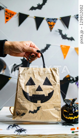 Hand Holding Halloween Paper Bag with Jack O Lantern Design and Bat Decoration 129912082