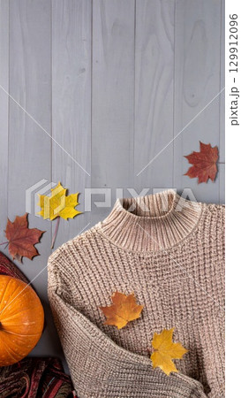Cozy Brown Sweater with Pumpkin and Colorful Fall Leaves on a Gray Wooden Table 129912096
