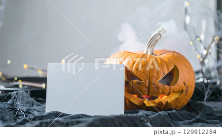Carved Orange Halloween Pumpkin with Greeting Card on Black Cloth with Festive Lights 129912284