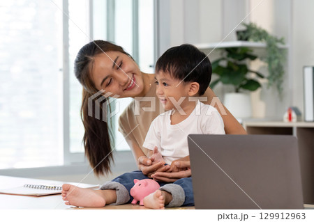 Mother and child enjoying financial literacy at home with piggy bank Mother and child enjoying financial literacy at home with piggy bank 129912963