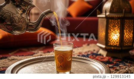 Pouring hot moroccan mint tea into a traditional glass on a silver tray in a cozy room Pouring hot moroccan mint tea into a traditional glass on a silver tray in a cozy room 129913145