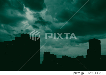 A dramatic cityscape at night features silhouettes of the buildings against moody sky with dark low clouds. Slhouetted district under overcast skyline A dramatic cityscape at night features silhouettes of the buildings against moody sky with dark low clouds. Slhouetted district under overcast skyline 129913359