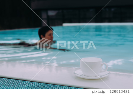 A person swims in a pool with a cup of coffee on the edge, enjoying a moment of relaxation A white cup and saucer sit on a pool edge, while a person swims A moment of peace and tranquility is captured A person swims in a pool with a cup of coffee on the edge, enjoying a moment of relaxation A white cup and saucer sit on a pool edge, while a person swims A moment of peace and tranquility is captured 129913481