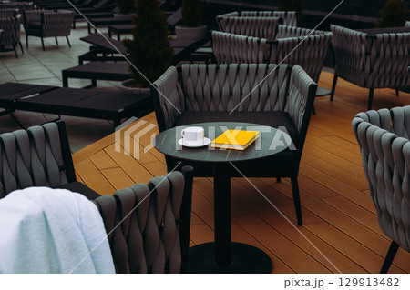 Cozy outdoor seating area, perfect for a relaxing morning with a cup of coffee and a book. A relaxing outdoor setting with a table, coffee and a book Cozy outdoor seating area, perfect for a relaxing morning with a cup of coffee and a book. A relaxing outdoor setting with a table, coffee and a book 129913482
