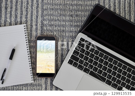 カーペットの上に置いたノートパソコンとスマホと筆記用具 129913535