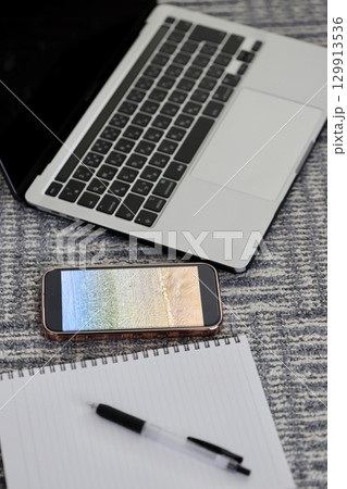 カーペットの上に置いたノートパソコンとスマホと筆記用具 129913536