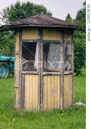 Old wooden shelter stands in a green field beside a tractor on a sunny day in a rural area Old wooden shelter stands in a green field beside a tractor on a sunny day in a rural area 129913610