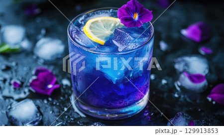Vibrant blue cocktail with lemon slice and purple flower garnish on icy surface 129913853
