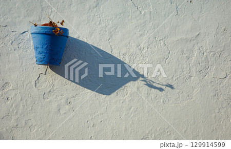 Blue flower pot on white wall with long shadow in Andalusian street 129914599