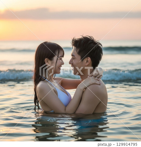 夕日の海に入り寄り添う日本人男女カップル 129914795