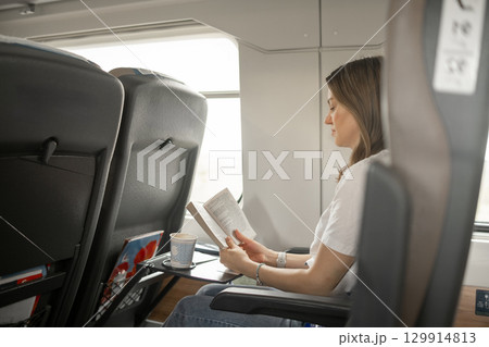 Reading a Book While Traveling on a Train in the Afternoon With a Cup of Coffee Beside Her Reading a Book While Traveling on a Train in the Afternoon With a Cup of Coffee Beside Her 129914813