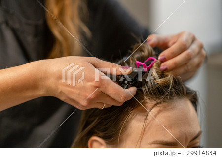 Hair coloring process in a salon with stylist using clips to secure curls during treatment 129914834
