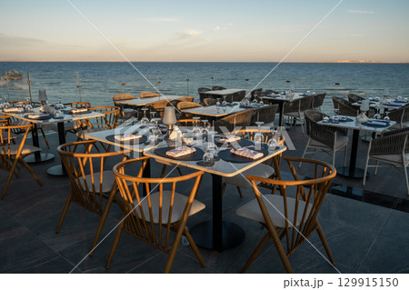 Golden sunset casts a warm glow over elegantly set tables at a seaside restauran 129915150