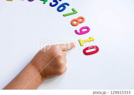 Child pointing at number sequence with colorful wooden numbers on white surface 129915353