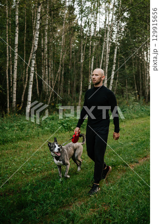 Man Walking Dog in Forest Path with Calm Expression 129915656