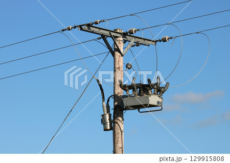 Electricity Pylon Pole with Electrical Wires Insulation and Switchgear Against a Blue Summer Sky 129915808