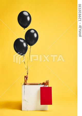 Child holding shopping bag and black balloons inside gift box on yellow background 129916530
