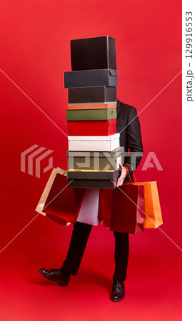 Person carrying boxes and paper shopping bags on red background Person carrying boxes and paper shopping bags on red background 129916553